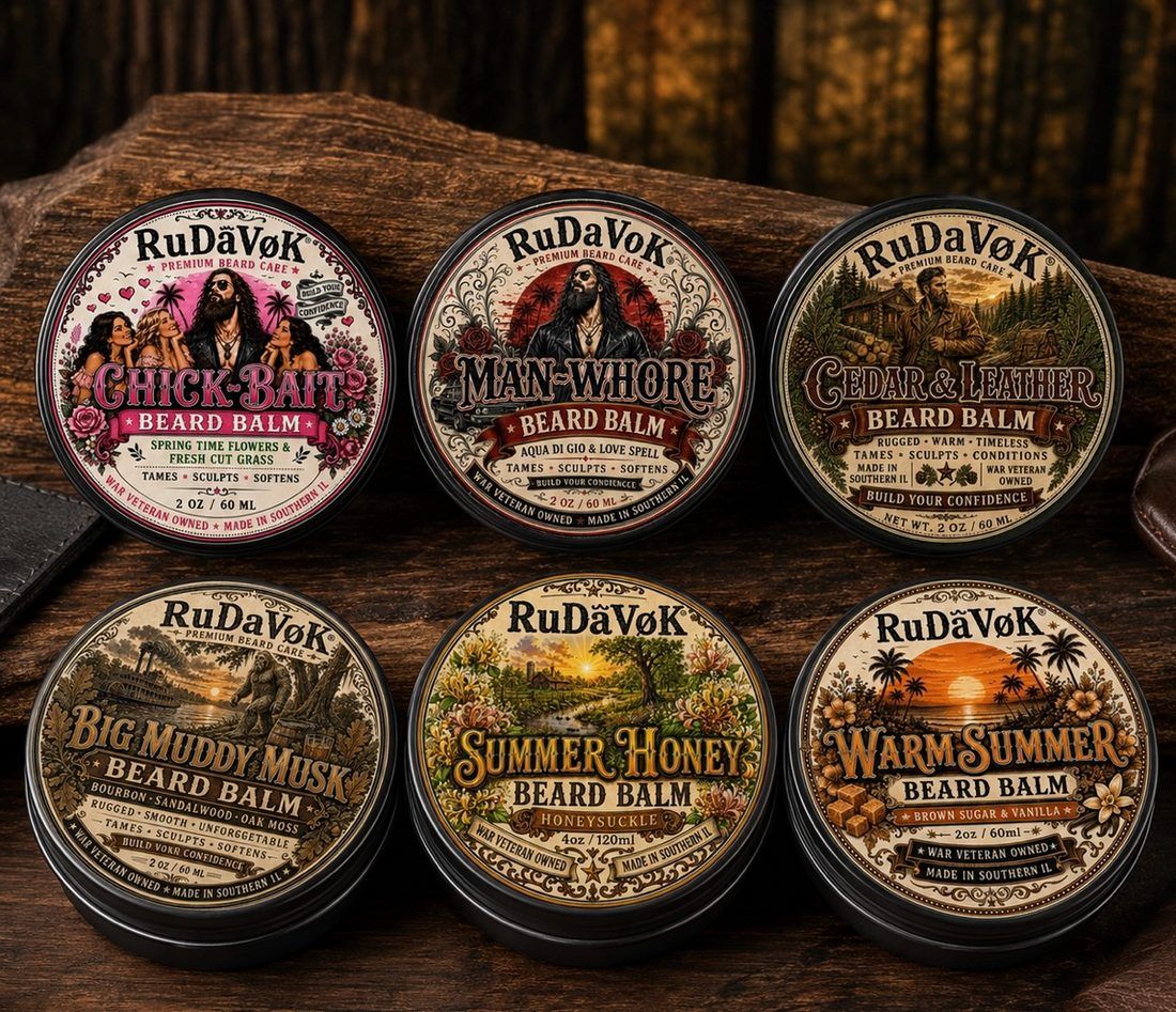 Real photo of six RuDaVoK beard balm tins arranged on a wooden surface — Chick-Bait, Man-Whore, Cedar and Leather, Big Muddy Musk, Summer Honey and Warm Summer
